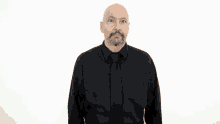 a bald man with a beard wearing a black shirt and tie is holding his hands up in the air