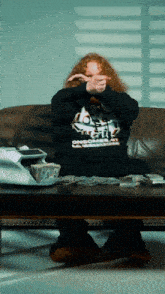 a man sitting on a couch covering his face with his hands and a sweatshirt that says one more time on it