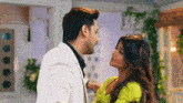 a man in a white suit and a woman in a green dress are looking at each other .