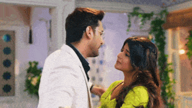 a man in a white suit and a woman in a green dress are looking at each other .