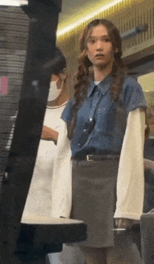 a woman wearing a mask and a denim shirt is standing next to a man .