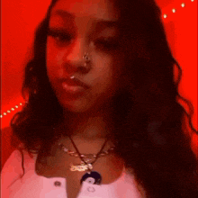 a woman wearing a nose ring and a necklace is standing in front of a red wall .