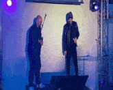 two men stand on a stage with microphones in their hands and one has a microphone in his right hand