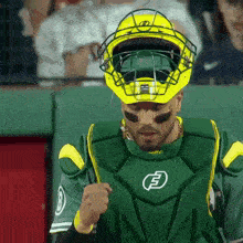 a baseball catcher wearing a green and yellow uniform with the letter b on it