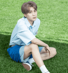 a young man in a blue shirt and blue shorts is sitting on the grass