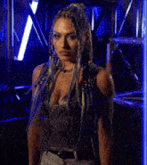 a woman with blue hair and braids is standing in a dark room in front of a blue light .