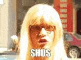 a woman wearing glasses and a blonde wig has the word shus on her face
