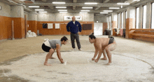 a man in a blue jacket stands between two wrestlers in a gym