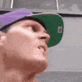a man wearing a purple hat and a green hat looks up at something .