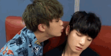two young men are sitting next to each other on a couch and one of them is kissing the other on the cheek .