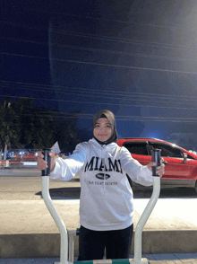 a woman wearing a miami sweatshirt is holding a cup