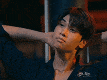 a young man with his hands behind his head is wearing a necklace and a black shirt .