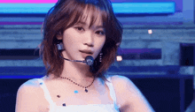 a woman wearing a microphone and a necklace is looking at the camera