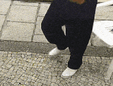 a person wearing black pants and white shoes is standing on a brick sidewalk