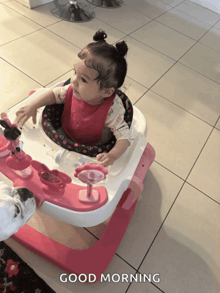 a baby is sitting in a pink and white walker with the words good morning on the bottom