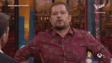 a man in a red shirt talks to another man on a tv show