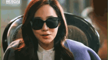a woman wearing sunglasses is sitting in a chair and looking at the camera .