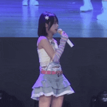 a girl is standing on a stage holding a microphone and wearing gloves .