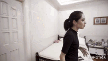 a woman in a black shirt is standing in front of a bed with the words made in animotica below her