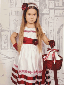 a little girl in a white and red dress holds a red basket