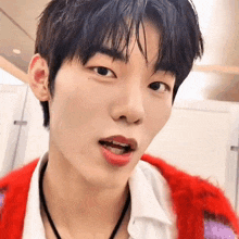 a close up of a young man wearing a red sweater and a white shirt with his mouth open .