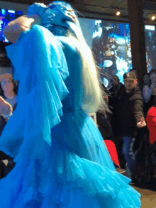 a woman in a blue dress is dancing in front of a crowd of people