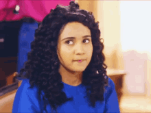 a woman with curly hair wearing a blue shirt is making a funny face