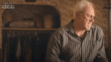 a man in a striped shirt and glasses is standing in a room with a light on .