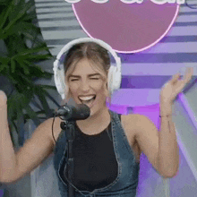 a woman wearing headphones is standing in front of a microphone and laughing .