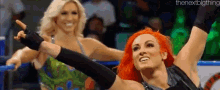 a couple of women are standing next to each other in a wrestling ring and one of them is pointing at the camera .