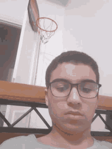 a man wearing glasses stands in front of a basketball net