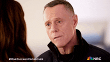 a man in a black jacket is talking to a woman with the nbc logo behind him