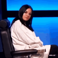 a woman is sitting in a chair wrapped in a white robe and looking at the camera .