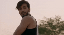 a man with a beard is wearing a black tank top and looking at the camera .