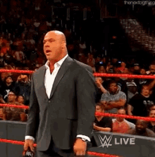 a man in a suit is standing in a wrestling ring with a crowd behind him .