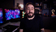 a man with a beard is sitting in front of a computer monitor and making a face .