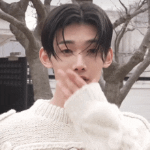 a young man wearing a white sweater covering his mouth with his hand