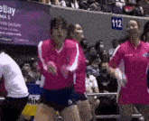 a group of women in pink shirts are dancing in front of a crowd with a sign that says elway on it