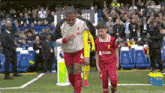 a soccer player in a red jersey is walking on the field with a young boy