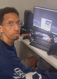 a man wearing glasses sits at a desk with a computer