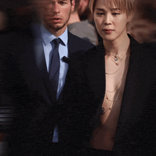 a man in a suit and tie is standing next to a shirtless man in a black jacket