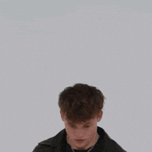 a young man wearing a leather jacket and a necklace is standing in front of a wall .