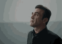 a man in a black shirt and tie looks up into the sky