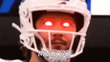 a man wearing a football helmet with red eyes and the words `` mvgoat '' written on his face .
