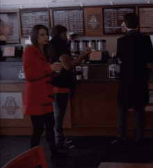 a woman in a red coat is standing in front of a counter with a sign that says ' coffee shop ' on it