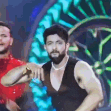 a man with a beard is wearing a black vest and a necklace