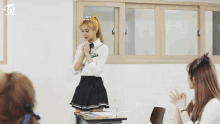 a group of girls are sitting at desks in a classroom with a twice logo on the wall