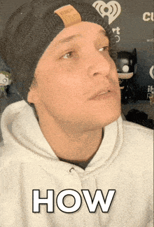 a man wearing a black beanie and a white hoodie says " how "