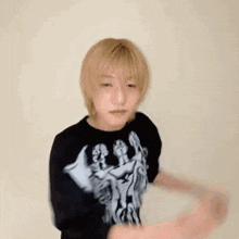 a young man with blonde hair is wearing a black t-shirt with a picture of a skeleton on it .