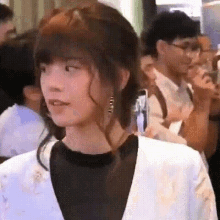 a woman in a white jacket and black shirt is standing in a crowd of people .